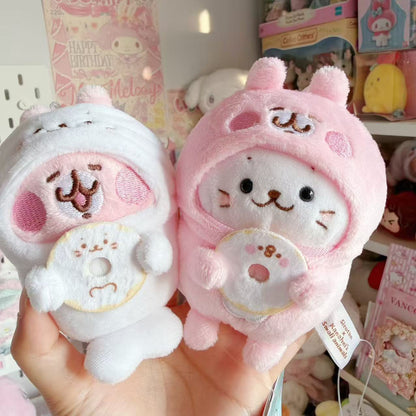 Sirotan × Kanahei’s Small Animals pink and white plush mascots held together, wearing swapped rabbit and seal costumes and holding character donuts.