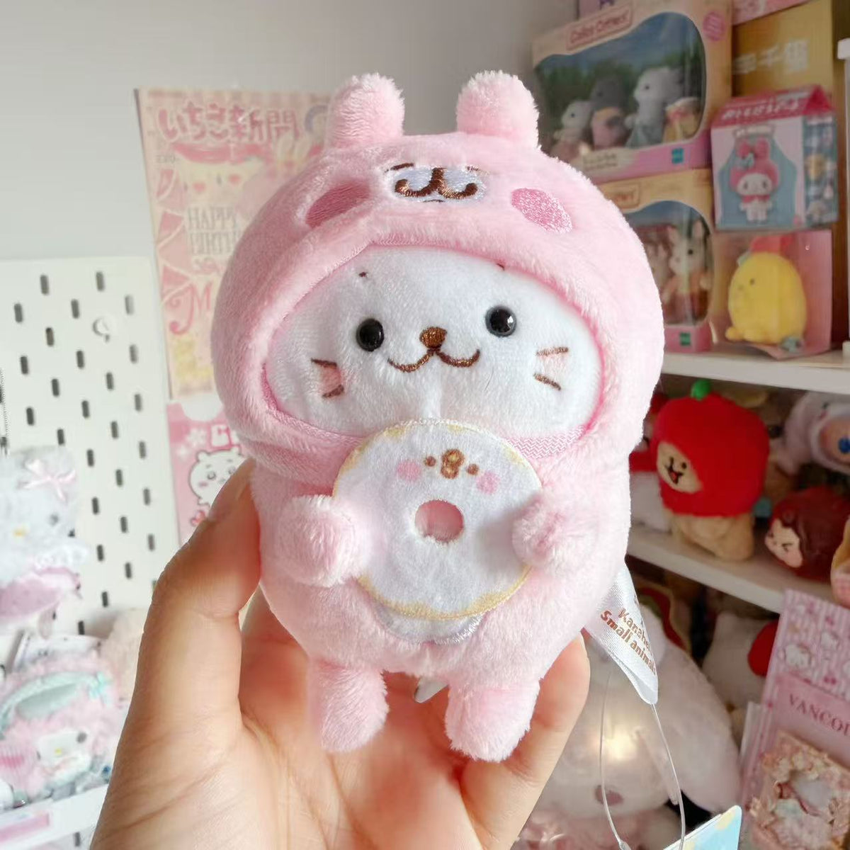 Sirotan white seal plush mascot wearing a pink Kanahei rabbit costume and holding a donut with a Piske face.